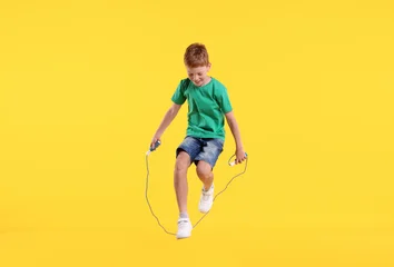 Cute little boy jumping with skipping rope on yellow background © New Africa