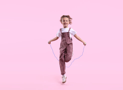 Cute little girl jumping with skipping rope on pink background