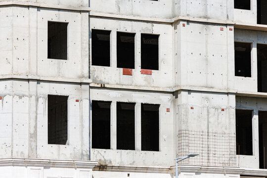 Unfinished concrete multi-story building facade with empty windows and exposed rebar