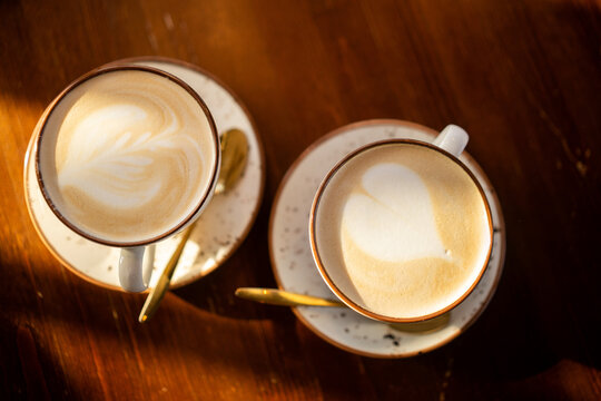 Two cappuccinos with latte art on wooden table in warm sunlight