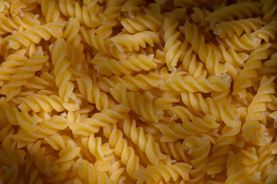 Commercial food photography of a macro top-down background of dry fusilli pasta with moody shadows