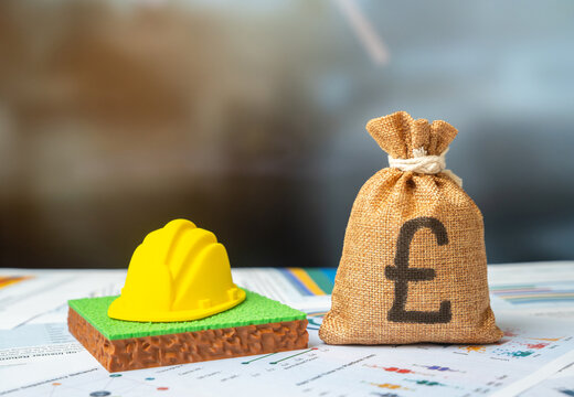 British pounds money bag and a plot of land with a hard hat. Selecting a site for construction. Construction budget.