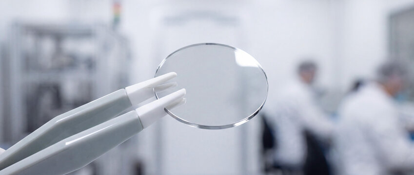 Close-up of a High Precision Optic Lens Held by Tweezers in a Modern Science Laboratory with Blurred Researchers