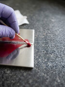 Inspector applying red dye penetrant with cotton swab onto welded stainless steel joint