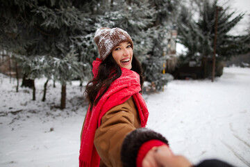 Fototapeta premium Laughing woman glancing back while holding hand, walking through snowy winter forest