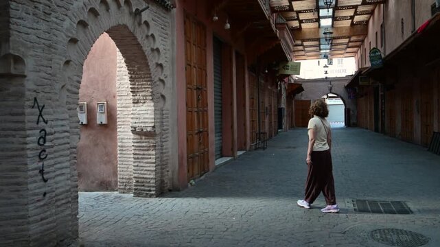 Marrakech, morocco. August 10, 2026. Solitary female tourist standing and then walking away through a deserted, narrow alley in the ancient medina of marrakech, morocco