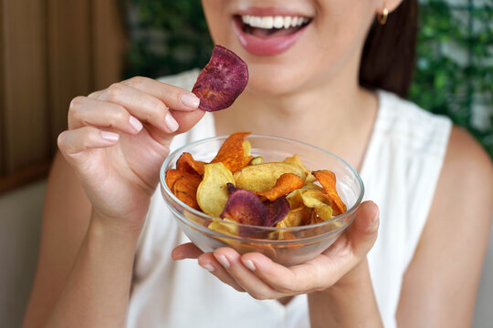 Healthy woman eating colorful sweet potato chips from bowl