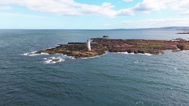 Aerial orbit tracking view of historic St Baldreds Cross on rocky coastal headland near North Berwick Scotland