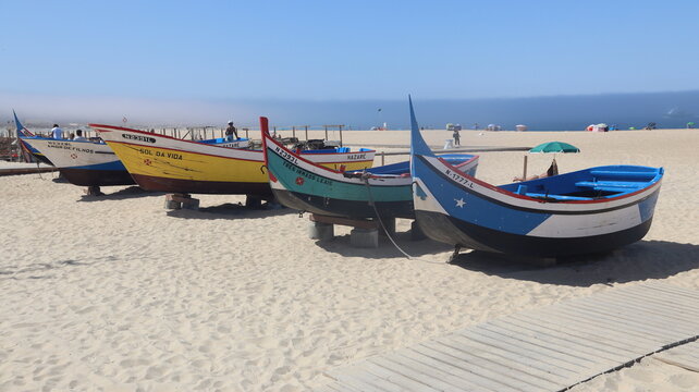 NAZAR&Eacute;, PORTUGAL - SEPTEMBER 8, 2026: General view of Nazar&eacute; coastal town and Atlantic Ocean Colorful fishing boats resting on a sandy beach under a clear blue sky