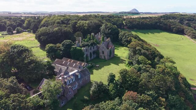 Aerial orbit continuation shot of ruined historic Seacliff House estate surrounded by woodland in Scotland