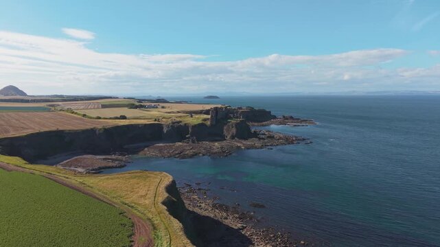 Drone view flying forward over rugged coastal cliffs and fields towards Tantallon Castle in East Lothian Scotland