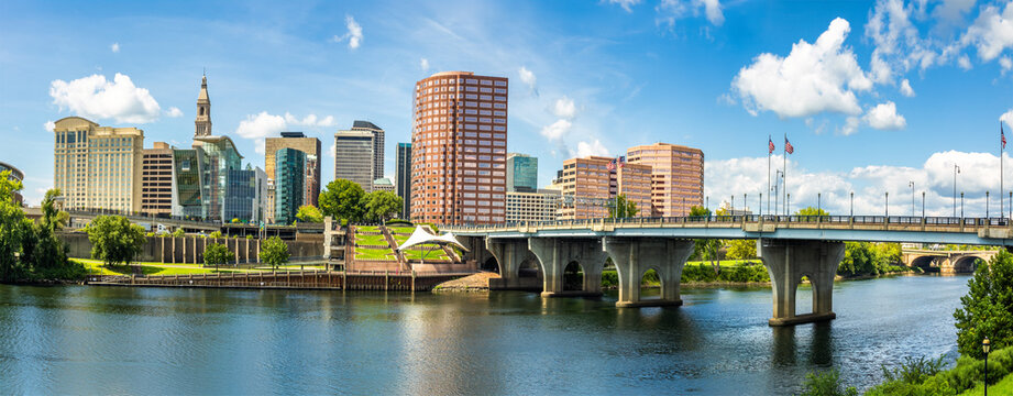 Hartford skyline panorama from across the Connecticut River on a sunny day, showcasing downtown buildings, the waterfront, and the capital of Connecticut.