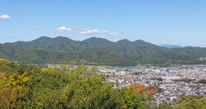 Panoramic view of Kyoto cityscape surrounded by green hills and distant mountains under wide blue sky with soft clouds, Kyoto, Japan