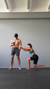 Athletic woman performs assisted single-leg squats while holding a man's hand for support. Balance, leg strength, stability and partner training concepts. Vertical video.