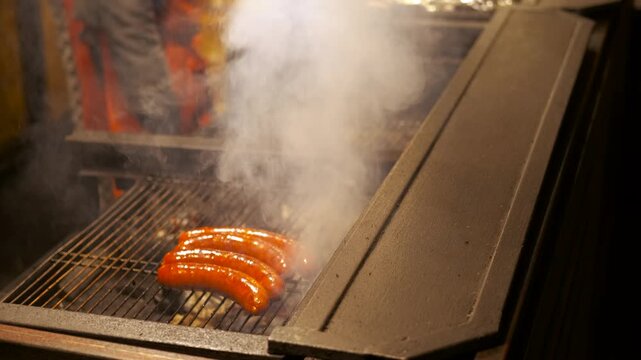 Street food vendor grilling sausages on a charcoal bbq. Professional cook grilling juicy pork bratwursts over smoky charcoal at a festive christmas market, turning sausages with tongs to serve