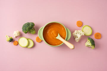Obraz premium Baby's first feeding: homemade vegetable puree in a silicone bowl with wooden spoon on pink background