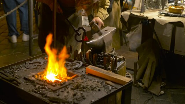 Blacksmith forging metal on an anvil with hammer. Artisan blacksmith using a hammer and anvil to shape a glowing hot metal piece taken from a forge with tongs, showcasing traditional metalworking