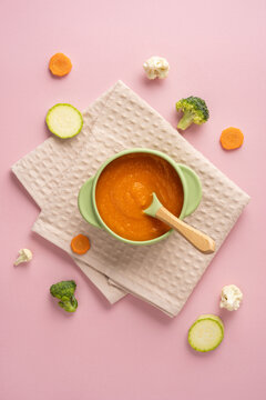 Baby's first feeding with carrot puree and healthy vegetable baby food in pastel vertical flatlay