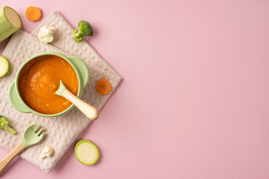 Baby's first feeding with healthy carrot puree in a green bowl on a pink background