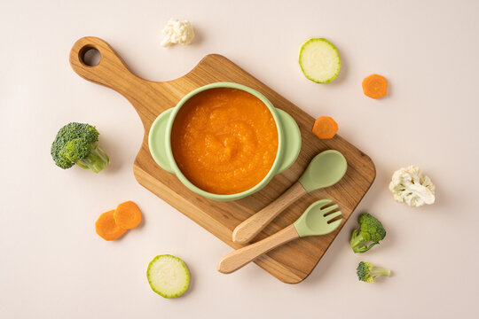 Baby's first feeding with healthy carrot puree in a green bowl on a wooden board