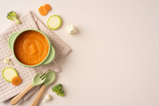 Baby's first feeding with healthy vegetable puree in green bowl with spoon on napkin
