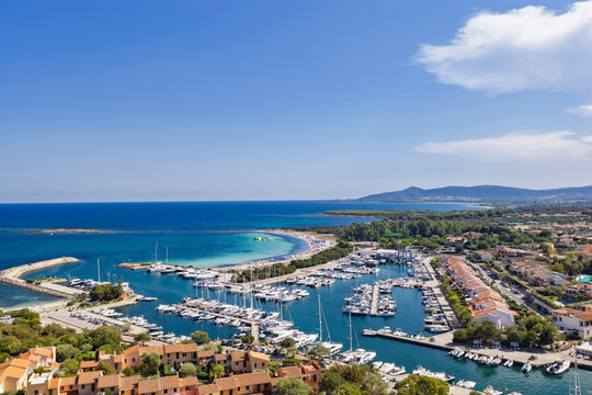 Aerial view of Porto Ottiolu marina and turquoise Mediterranean coastline in Sardinia, Italy, with yachts, sandy beach and coastal landscape under a clear blue sky