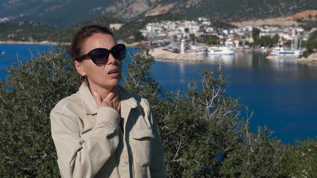 Asthma attack near the sea. Female tourist experiencing asthma attack managing respiratory symptoms while using inhaler near ocean coastline during summer day, struggling with breathing difficulty