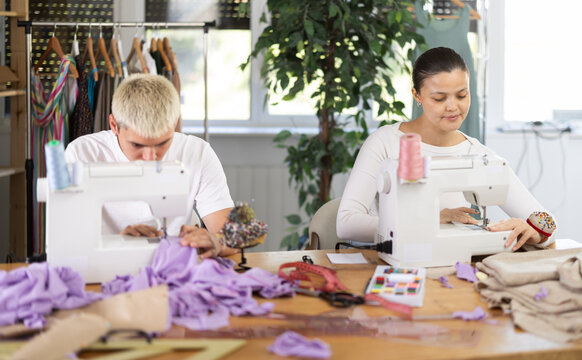 Tailors are working on a collection of clothes. Male tailor working in team with Asian female seamstresses, they sew the sample for approval with customer