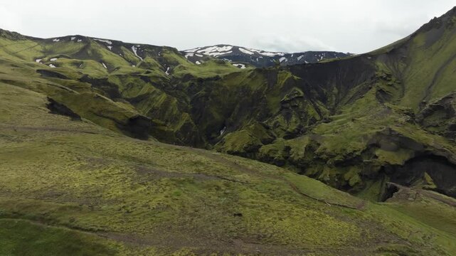 An aerial drone shot booms up and pushes in on the Fimmv&ouml;r&eth;uh&aacute;ls hiking trail on Iceland. The volcanic landscape with deep canyons, cliffs, and distant snow patches unfolds under an overcast sky.