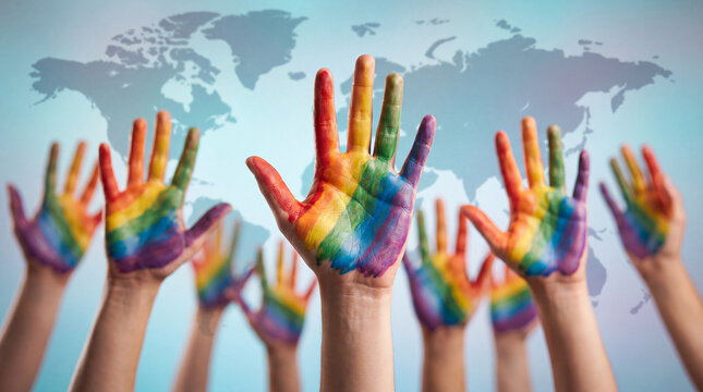 A group of diverse people raising hands painted with rainbow colors in support of equality, human rights, and LGBTQ+ pride against a global world map background.