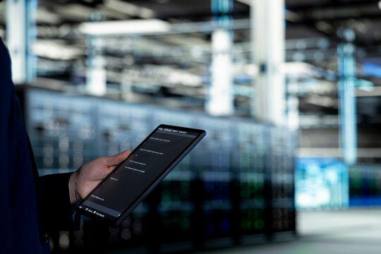 Data center programmer codes on a tablet while upgrading autonomous IT infrastructure rigs; the software developer uses a programming script app on a touchscreen device to update systems.