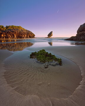 Wet sand, rocks, tidal pools, 'El Pic&oacute;n' limestone p&igrave;nnacle, Playa de Buelna Beach at low tide on a spectacular, fiery dawn. Llanes-Asturias-Spain-082