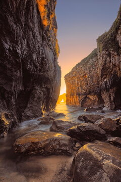 Tide uprush inside the narrow, rock-dotted Playa la Canalina Beach backed by a fiery dawn over Castro de las Gaviotas islet. Llanes-Asturias-Spain-088