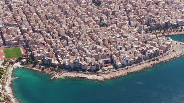 High-angle view showcasing the densely populated city of Piraeus in Greece, with its characteristic buildings and urban planning extending right to the edge of the turquoise Aegean Sea