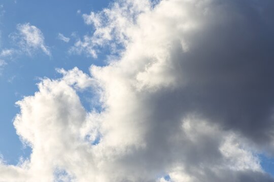 Dark storm clouds transitioning into sunlit white cumulus clouds in blue sky
