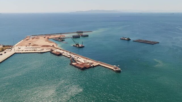 Impressive aerial perspective of a new port under construction with heavy machinery, barges, and cranes building a breakwater to create a safe harbor for maritime transport and industry