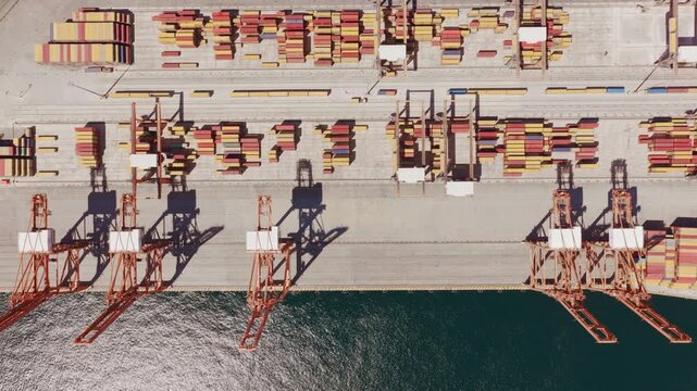 Expansive aerial perspective of a bustling commercial port, showcasing rows of colorful shipping containers and large gantry cranes poised along the wharf, capturing the scale of global trade