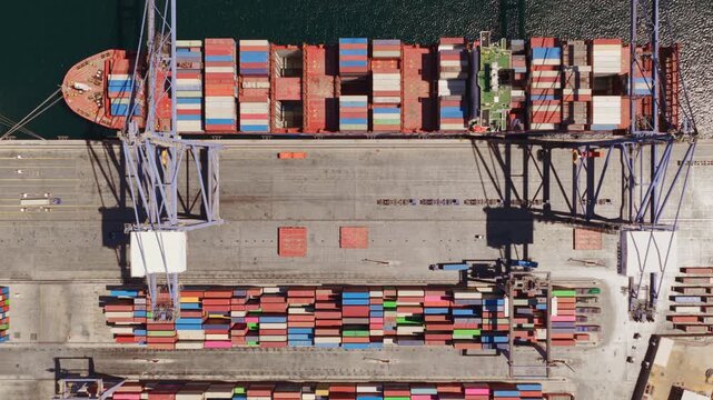 Aerial top-down view of a large container ship docked at a port with multicolored containers on its deck spelling the word help, representing a call for assistance in the shipping industry