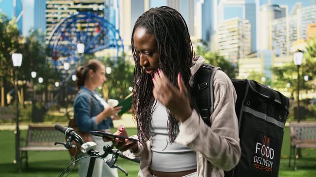 Courier fidgets while checking a food delivery app for a new order, waiting impatiently for a work request and showing anxiety about gig-economy work.