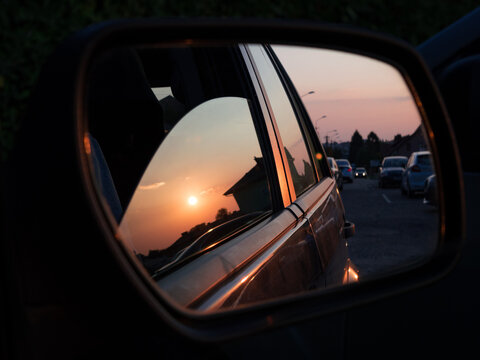 Golden sunset sky and sun reflected in a car side mirror during an evening road trip drive