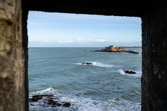 Scenic view of Fort National offshore fortress framed through a stone window in Saint-Malo, Brittany, France