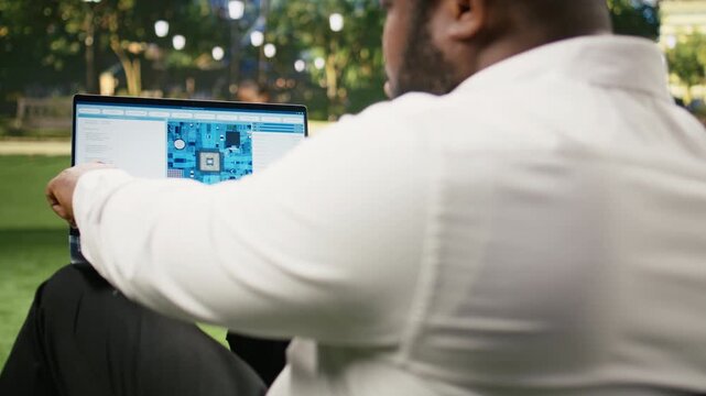 Businessman uses software with a microchip and circuit board interface on a laptop in a city park, illustrating semiconductor engineering and hardware monitoring during remote work outdoors.