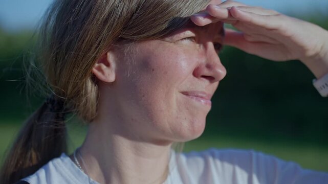 Closeup of woman shading her eyes with one hand while squinting in strong sunlight outdoors