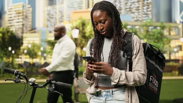 Smiling delivery courier holding mobile phone and thermal bag