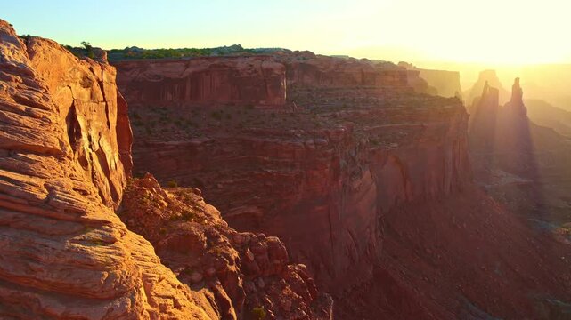 Early morning sunbeams illuminate Washer Woman and sandstone canyon cliffs viewed from Mesa Arch trail in Utah