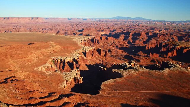 Golden evening sunlight illuminates rugged desert canyons and spires viewed from the White Rim Overlook trail in Utah