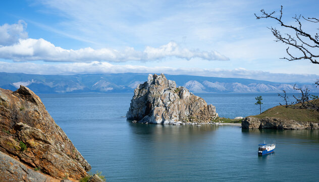 Landscape view of Shamanka Rock on Olkhon Island in Lake Baikal. Small passenger boat anchored in the bay with distant mountains under a blue sky. Natural Siberian landmark