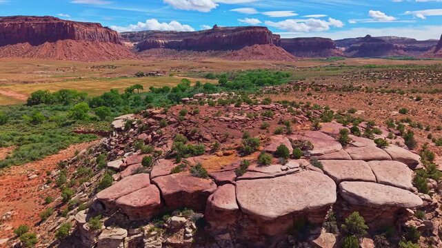 Weathered sandstone slabs overlook the green desert valley and towering red mesas along Indian Creek near Canyonlands Utah