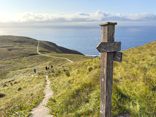 Wooden trail signpost and hikers on the coastal path at Runde © versus_cz