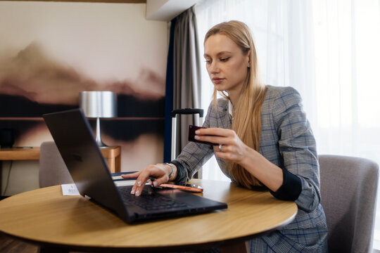 Entrepreneur holding bank card beside open laptop on a business trip. A close view focuses on digital finance and mobile work.